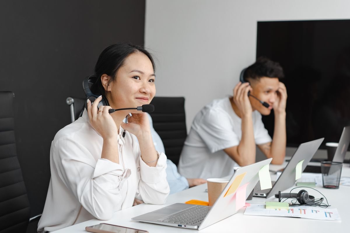 A front-desk agent on a headset taking a client call while a colleague works behind her