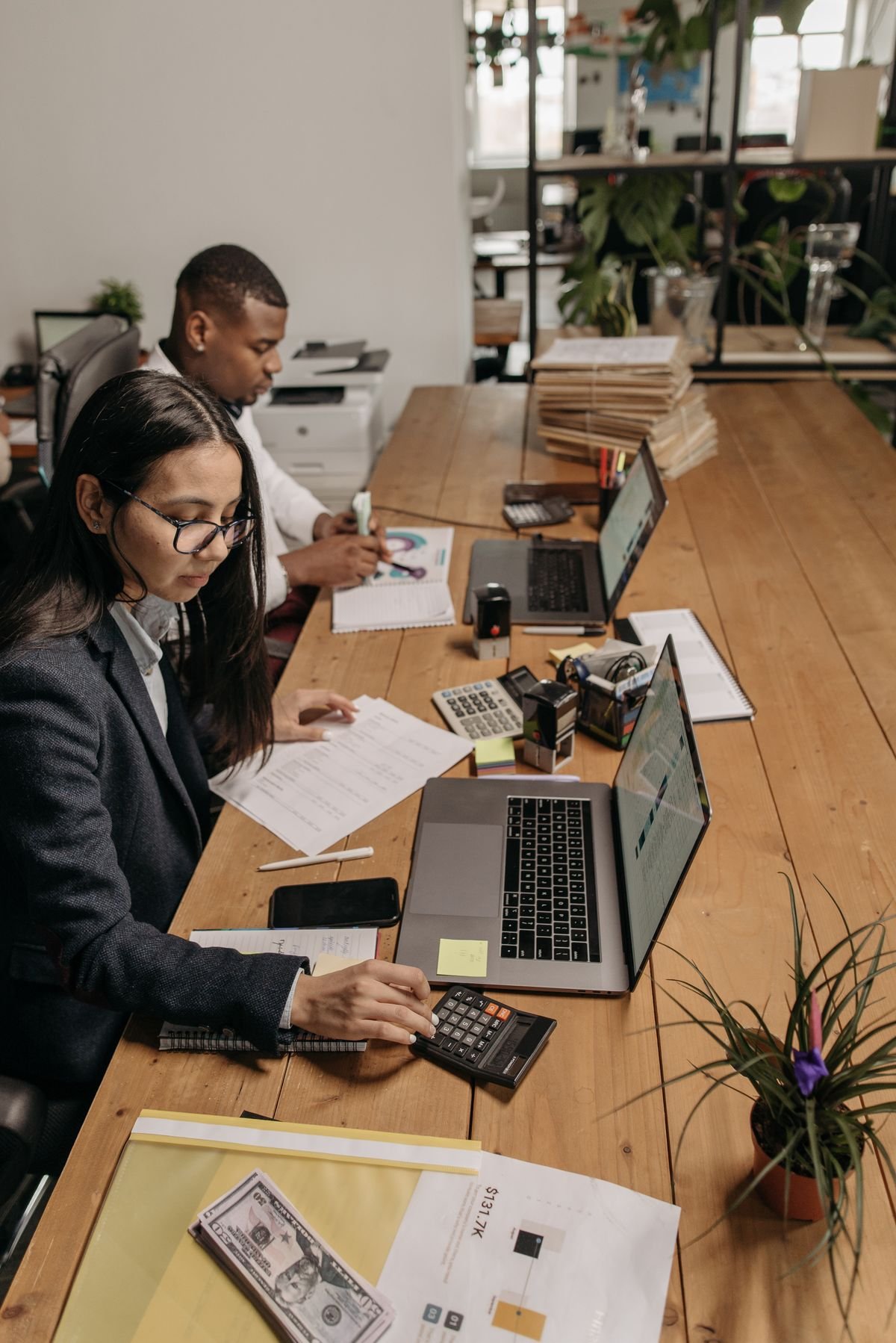 Two accountants working side by side at a shared desk covered in client documents